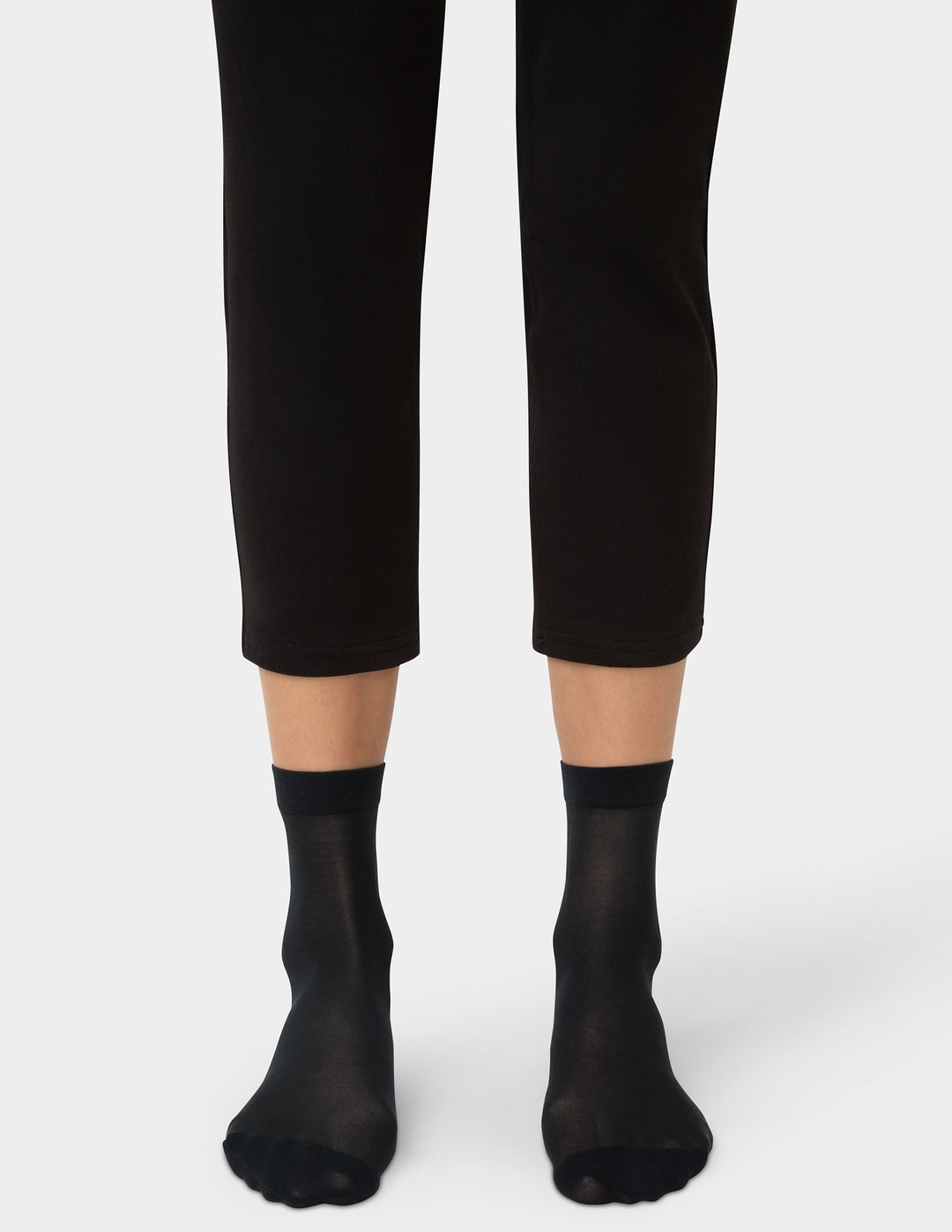 Person wearing black ankle socks and black pants on a white background