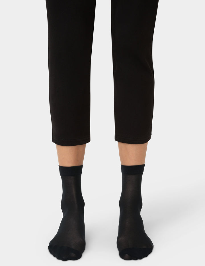 Person wearing black ankle socks and black pants on a white background