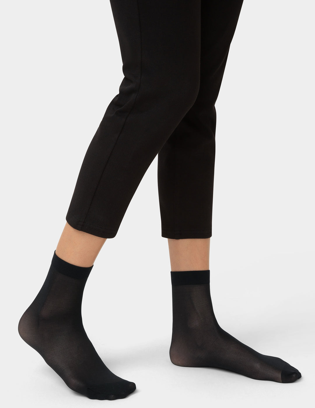 Person wearing black ankle socks and black pants on a white background