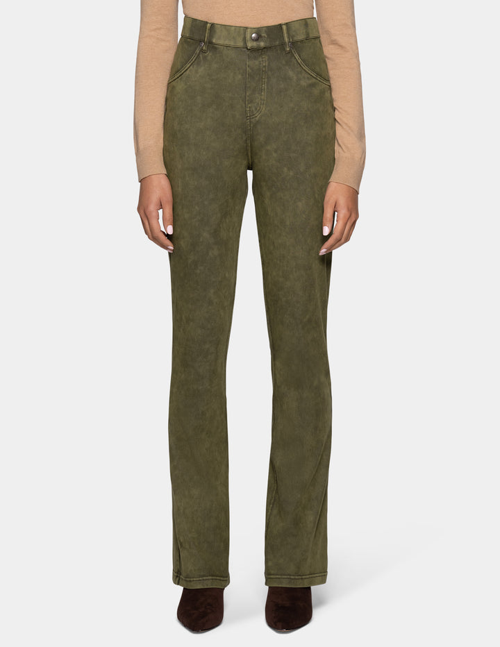 A model wearing olive green bootcut jeans, styled with a beige long-sleeve top and dark brown pointed-toe boots against a light gray background.