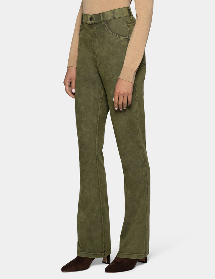A model from the side wearing olive green bootcut jeans, styled with a beige long-sleeve top and dark brown pointed-toe boots against a light gray background.