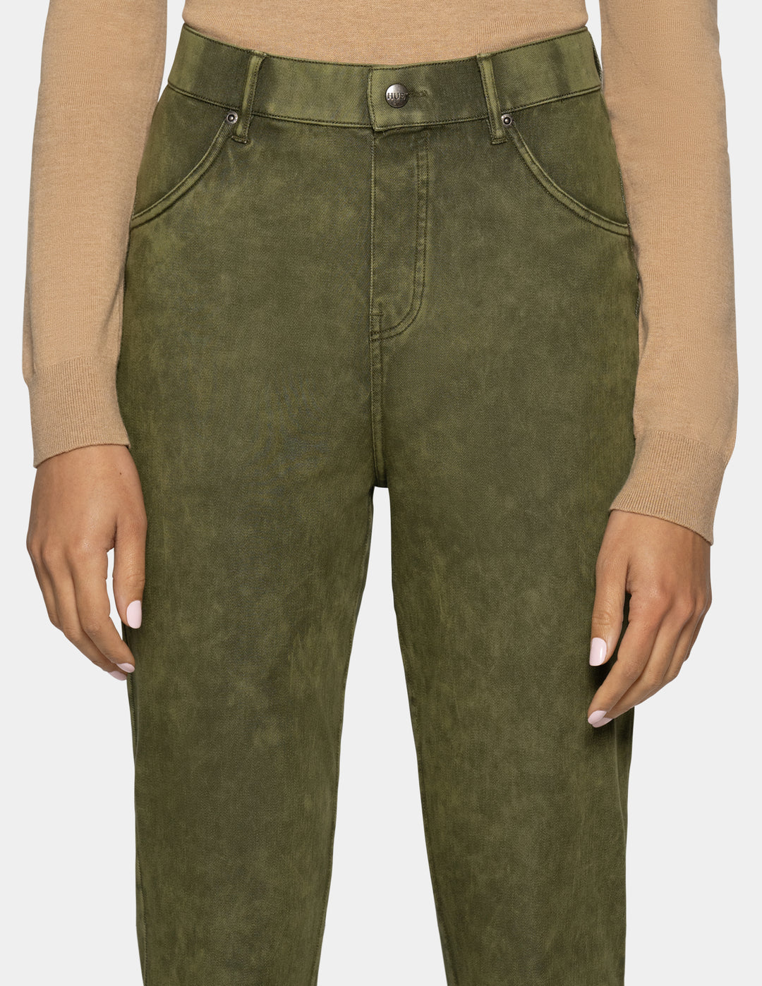 A close-up of a person wearing olive green high-waisted jeans with a washed finish, paired with a beige long-sleeve top against a light gray background.