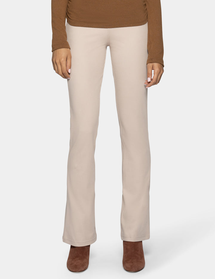 A model is shown from the waist down wearing light beige straight-leg pants, a brown long-sleeve top, and brown suede ankle boots against a light gray background.