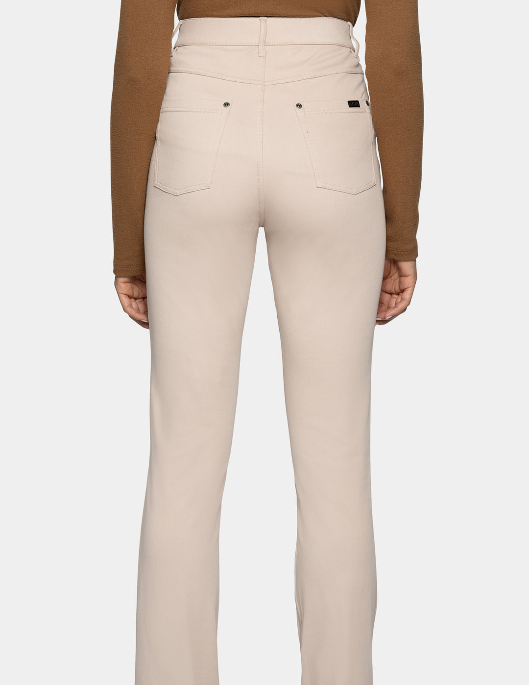 Rear view of a model wearing high-waisted beige pants with a brown long-sleeve top, shown against a light gray background.
