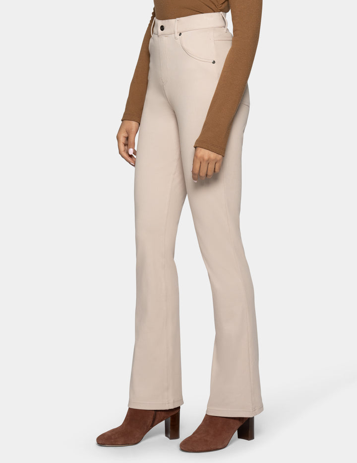 A model wearing high-waisted, light beige flared jeans with a brown long-sleeve top and brown heeled ankle boots, shown from the waist down on a light gray background.