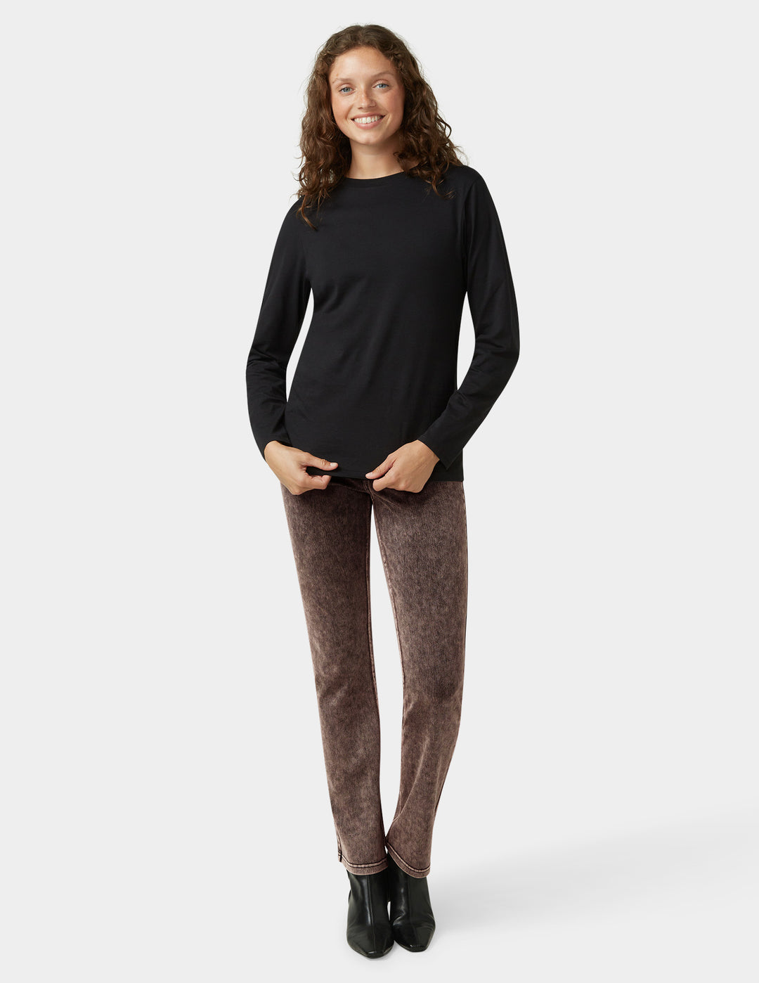 Woman wearing a black long-sleeve top and brown pants on a white background