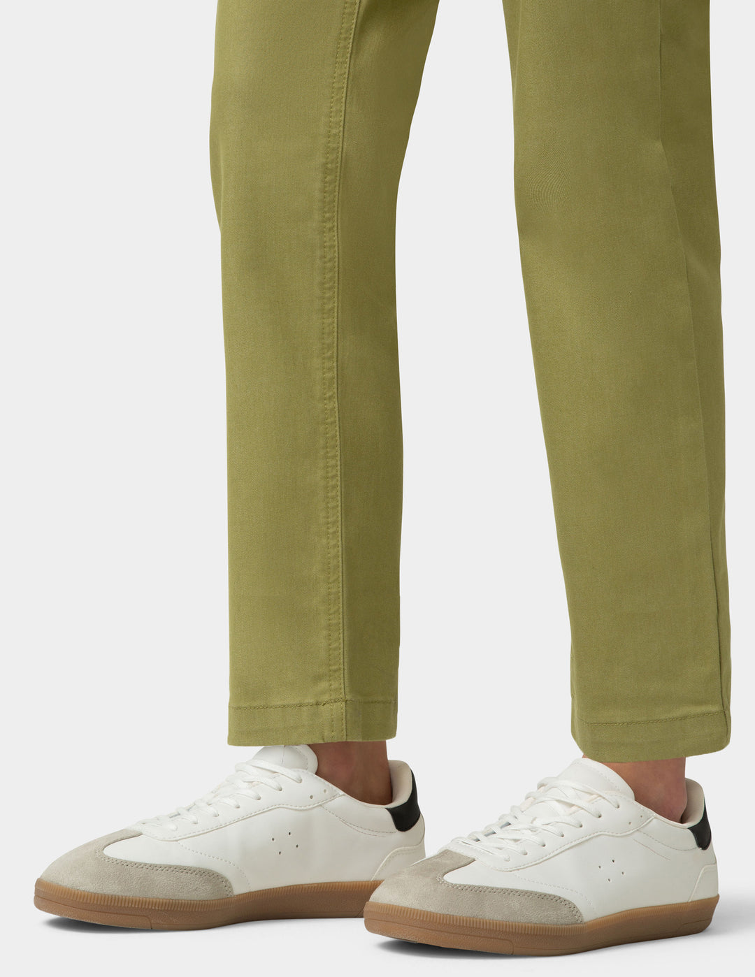 White sneakers with brown soles worn with green pants on a white background
