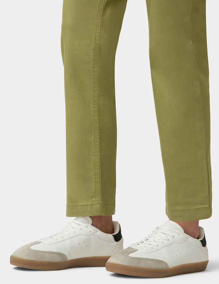White sneakers with brown soles worn with green pants on a white background