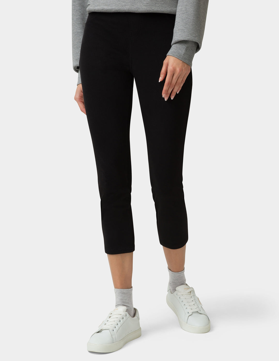 Person wearing black leggings with a gray sweater and white sneakers on a white background