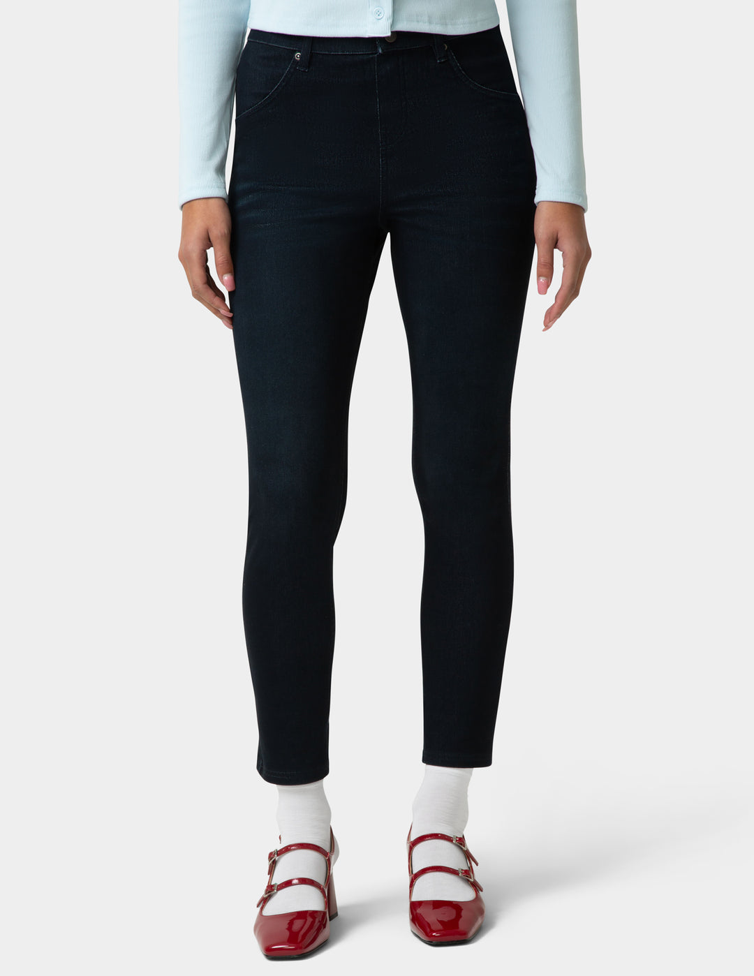 Person wearing black jeans with a light blue top and red shoes on a white background