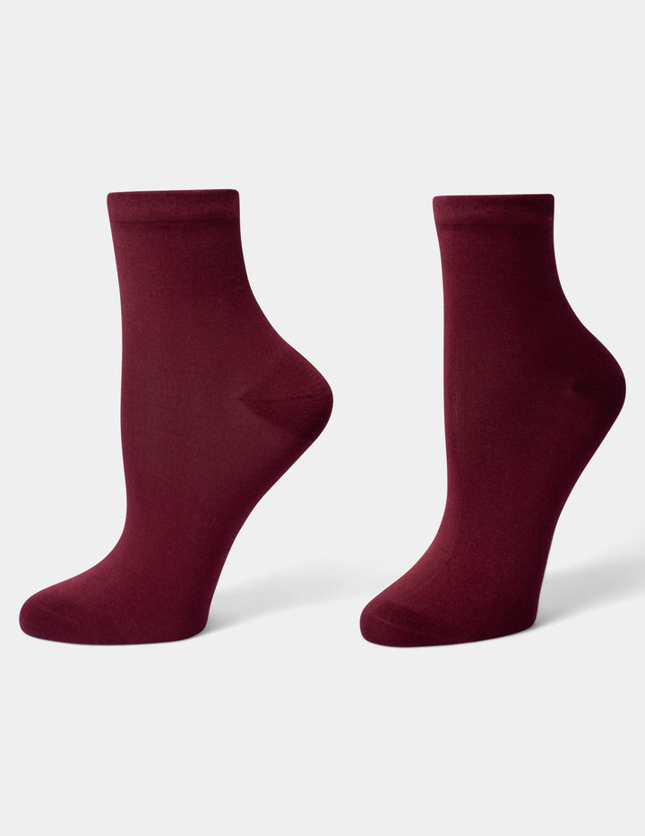 A pair of crew-length socks in a deep burgundy color, displayed on foot forms against a clean, light gray background.