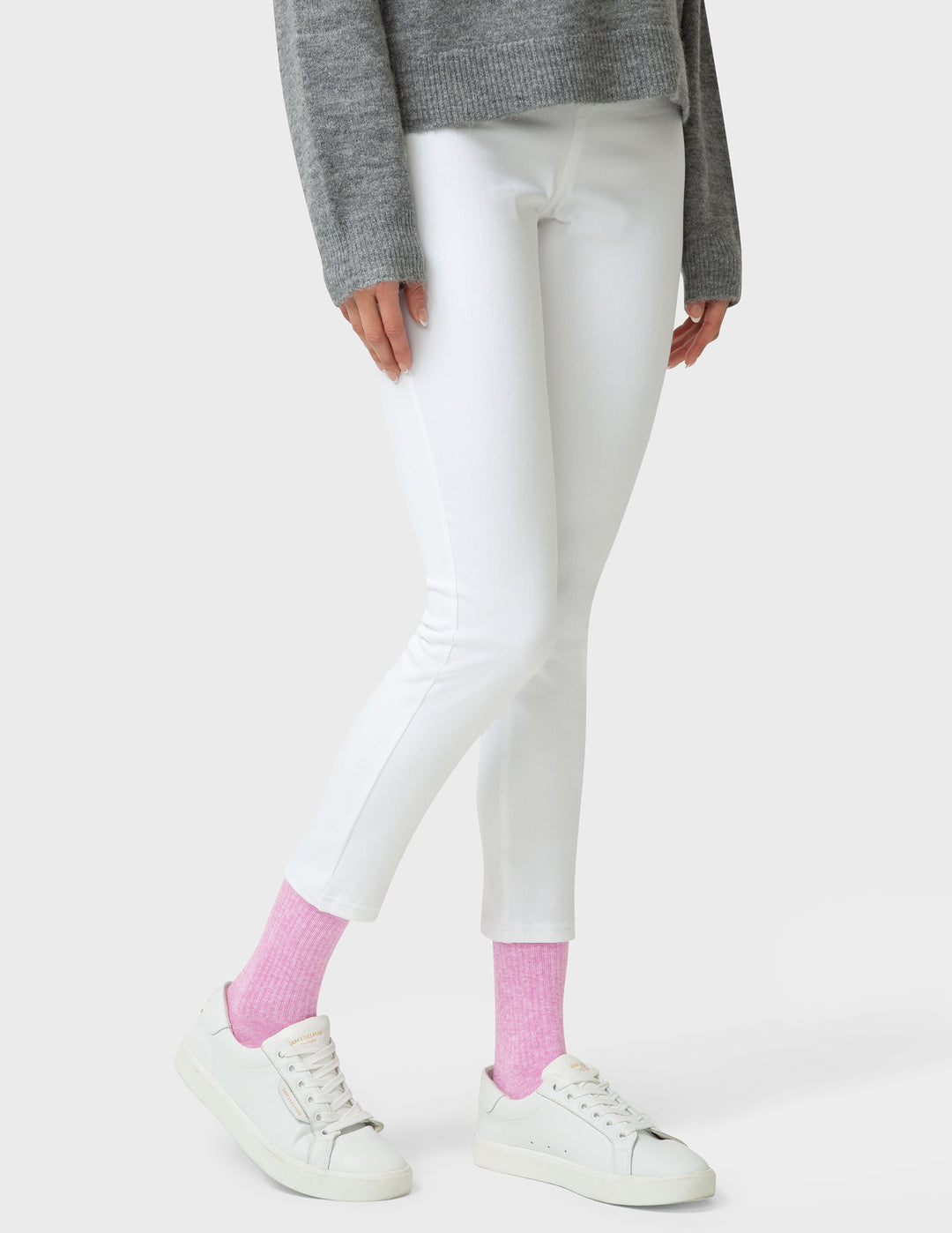 Person wearing white leggings, gray sweater, and pink socks on a white background