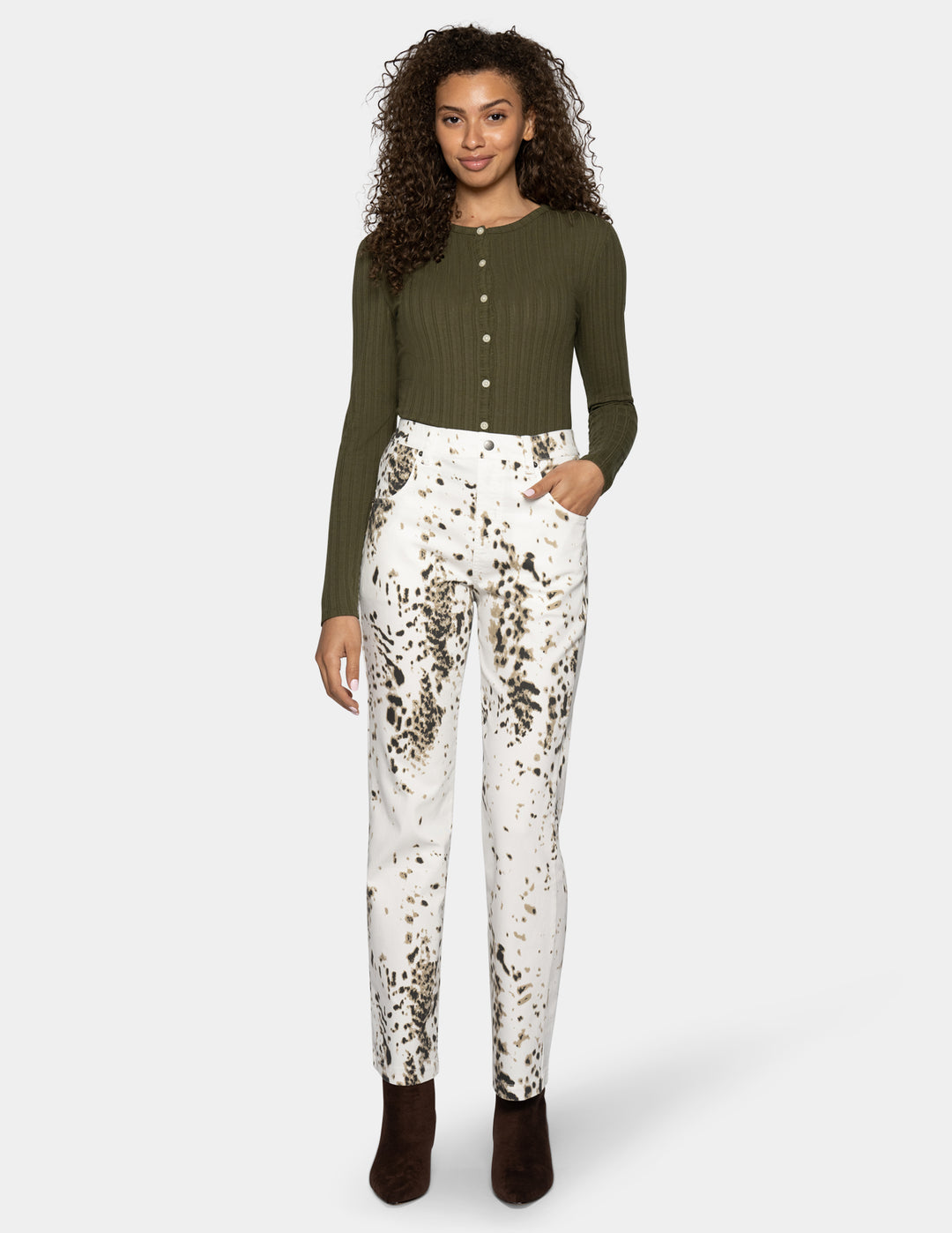 A woman modeling white straight leg pants with a brown animal print pattern throughout, paired with a long sleeve green top.