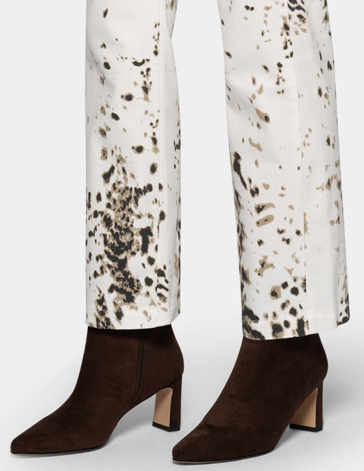 A close-up of a woman's legs wearing straight leg pants with a brown and black animal print on a white base, paired with dark brown suede ankle boots with block heels.