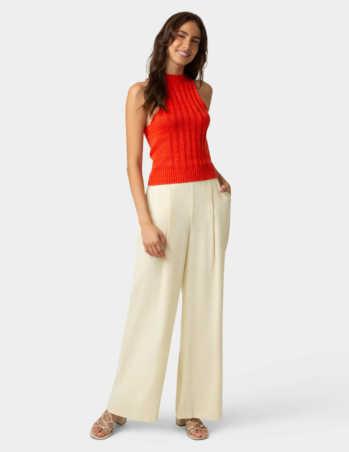 Woman wearing a red sleeveless top and beige pants on a white background