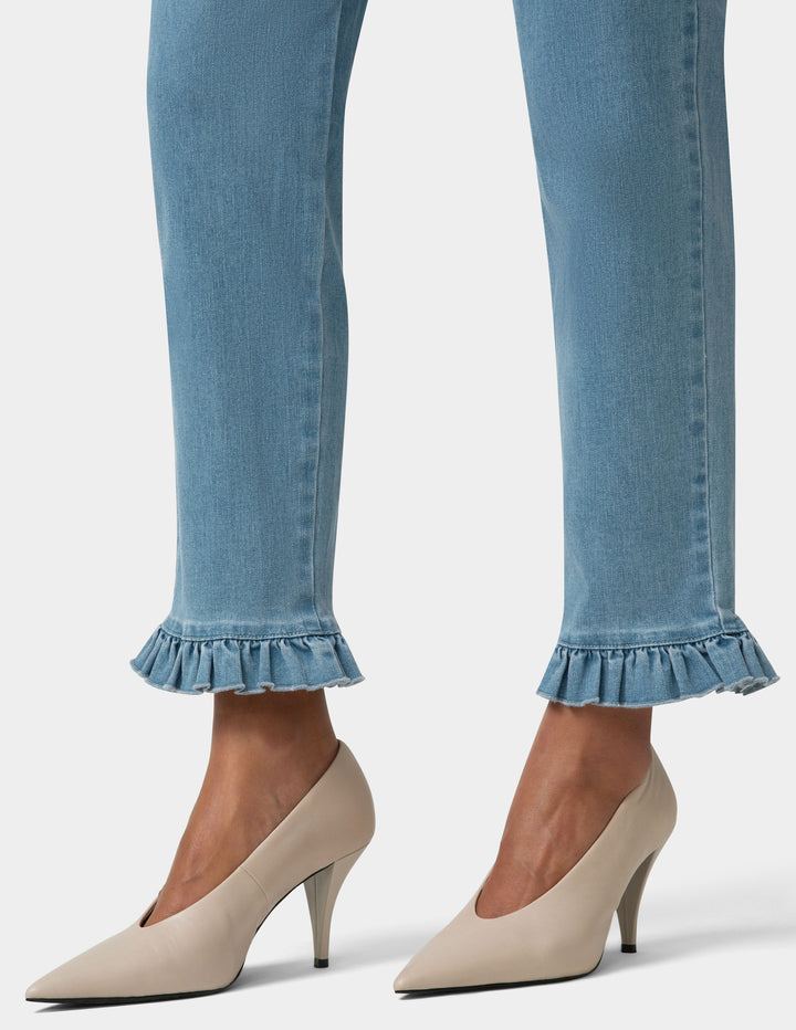 Blue jeans with ruffled cuffs worn with beige high heels on a light gray background