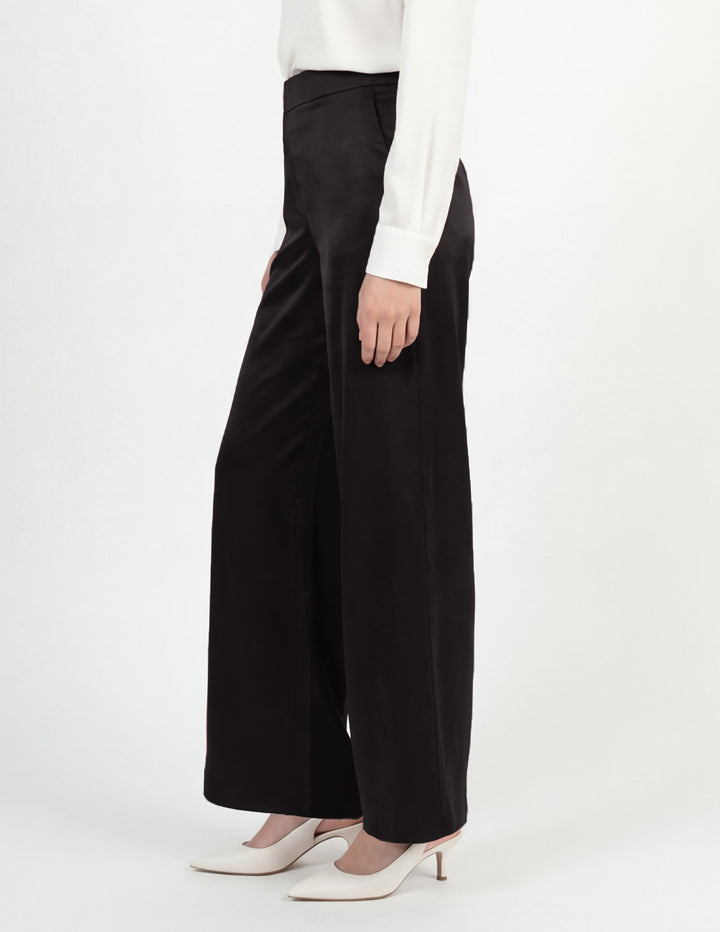 Person wearing black wide-leg pants with a white top on a white background