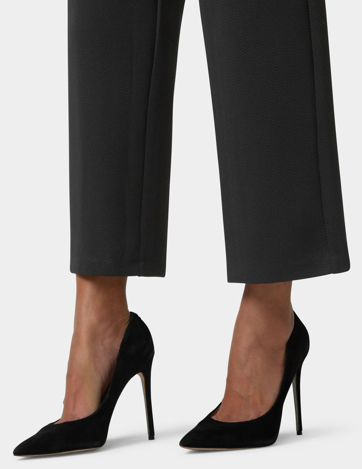 Black high-heeled shoes worn with black pants on a white background