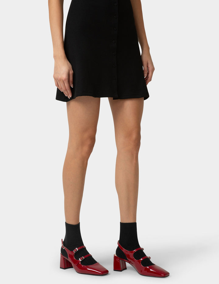 Person wearing a black dress, red shoes, and black socks on a white background