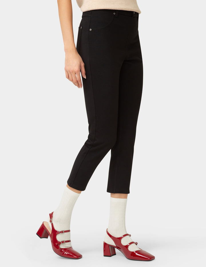 Person wearing black pants with red shoes and white socks on a light gray background