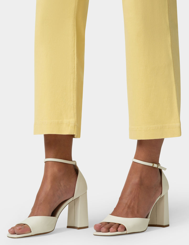 White block-heel sandals worn with yellow pants on a white background