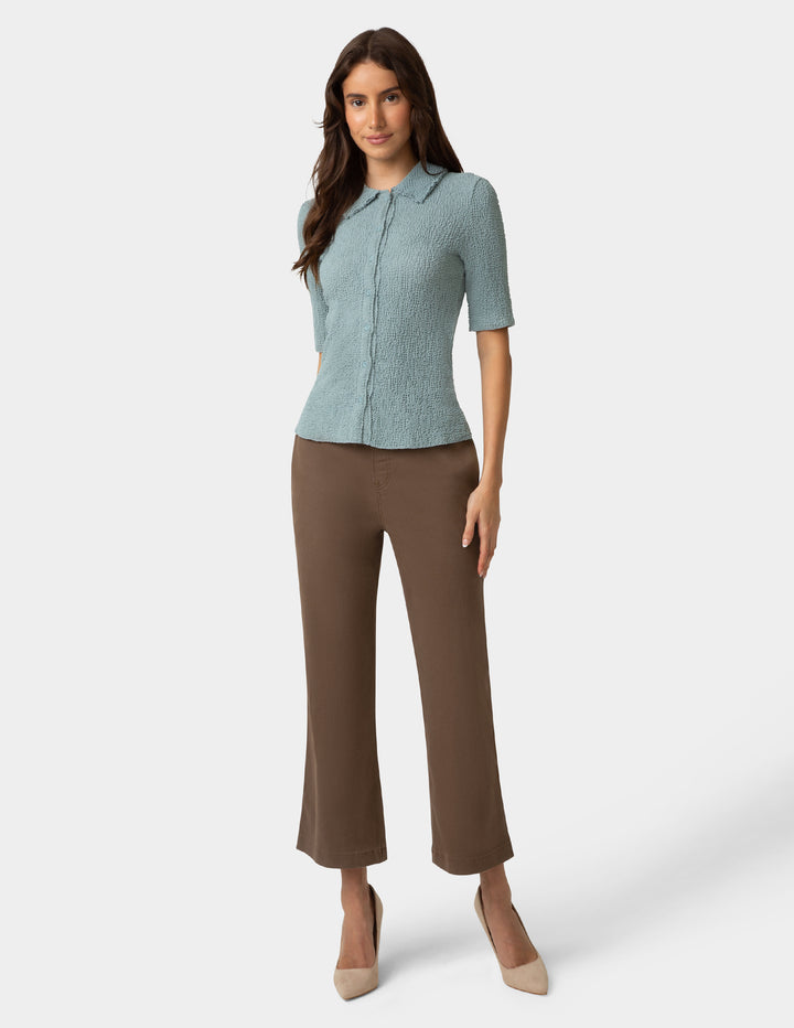 Woman wearing a light blue top and brown pants on a white background