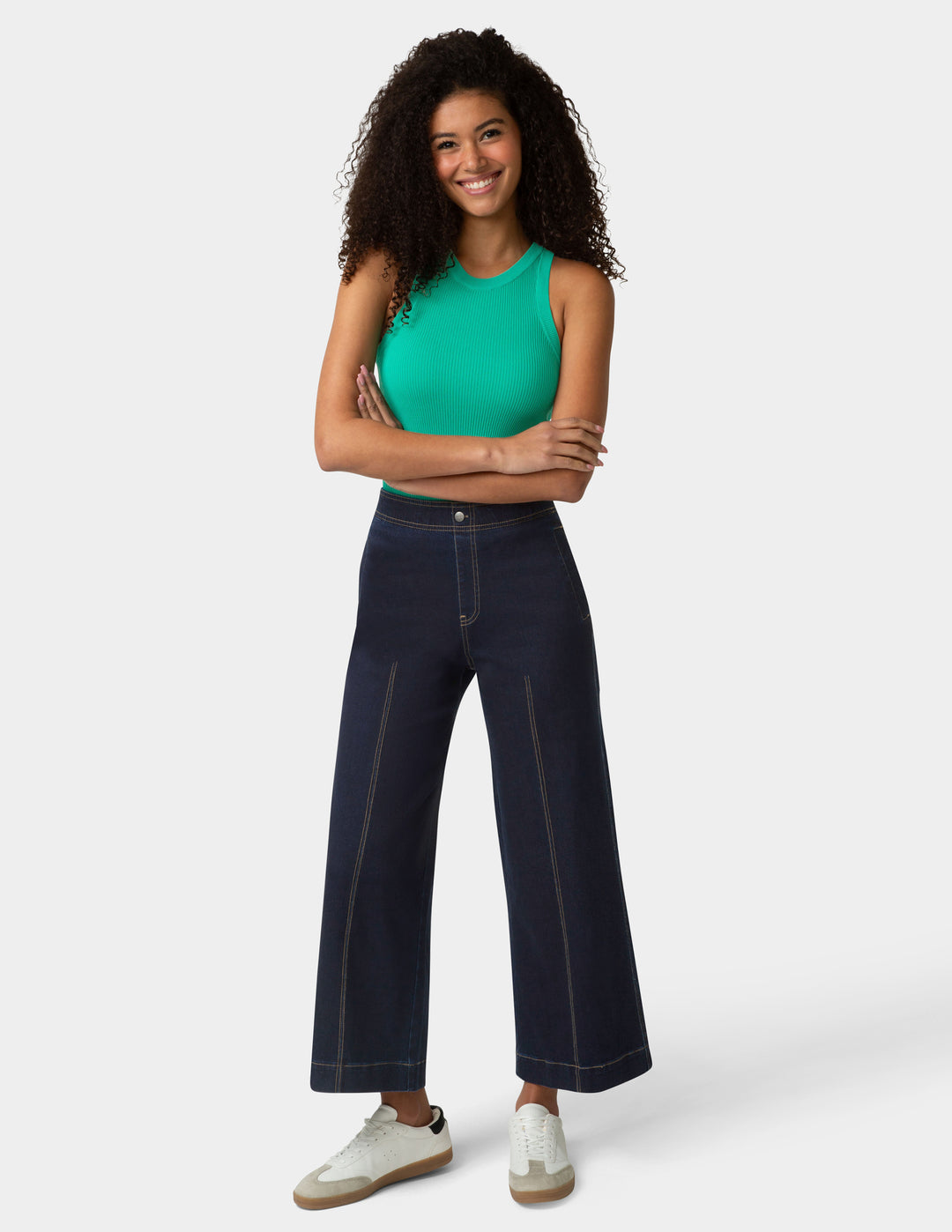 Woman wearing a green top and dark blue jeans on a white background