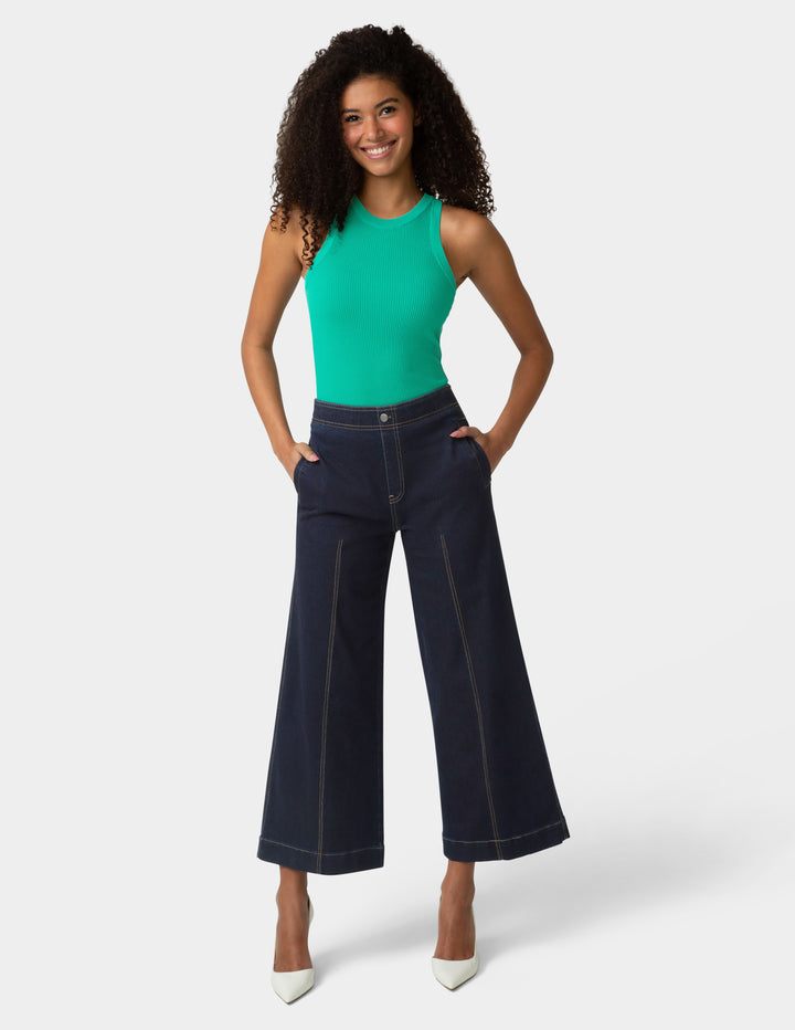 Woman wearing a green top and dark blue wide-leg jeans on a white background