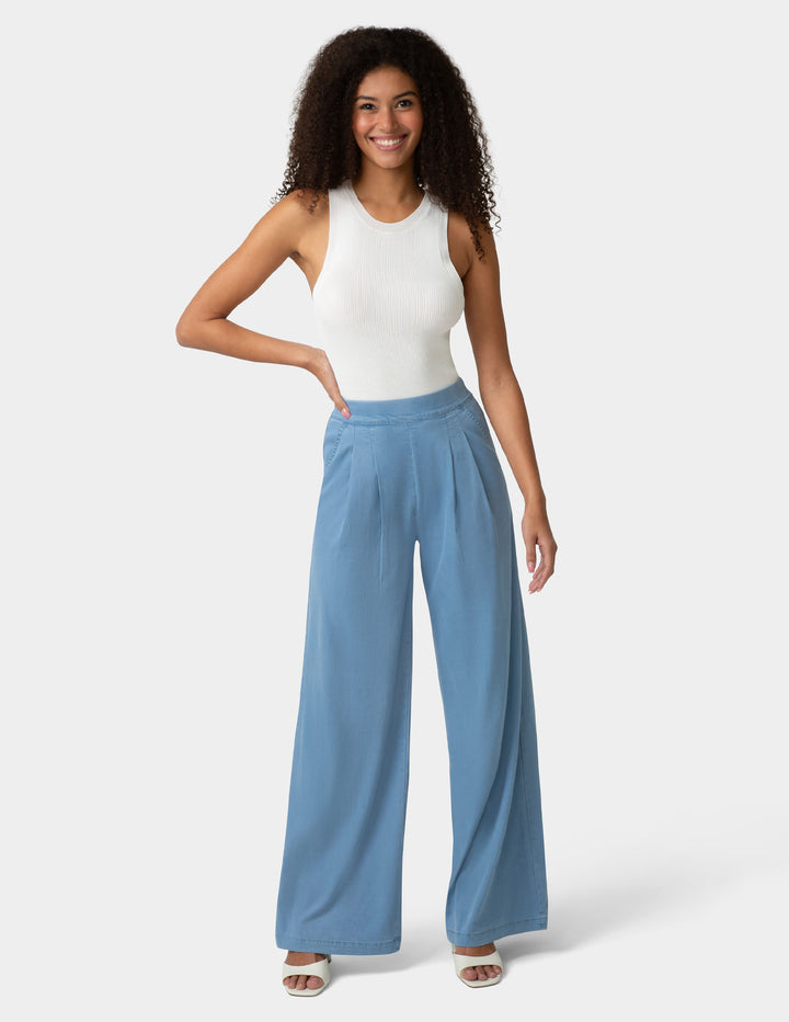 Woman wearing a white sleeveless top and blue wide-leg pants on a white background