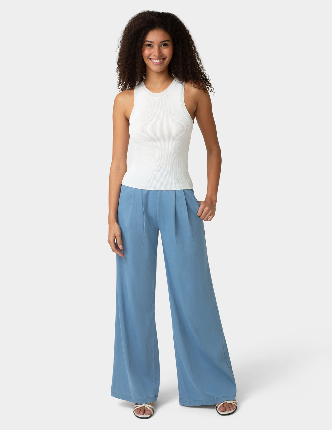 Woman wearing a white sleeveless top and blue wide-leg pants on a white background