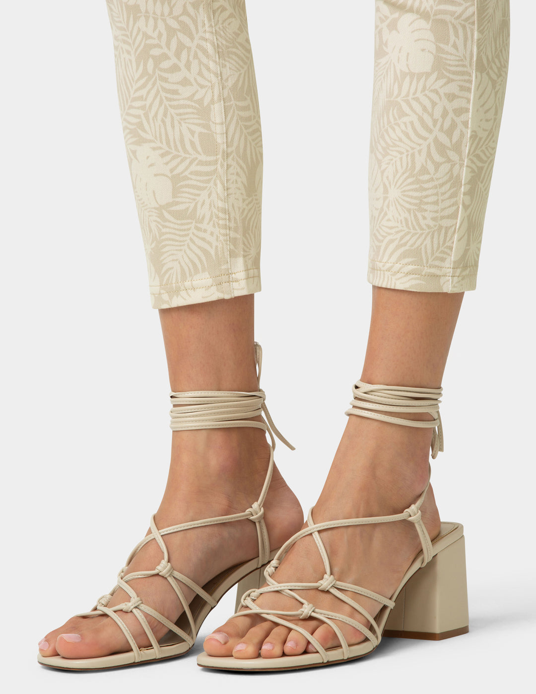 Beige strappy sandals worn with beige pants on a white background
