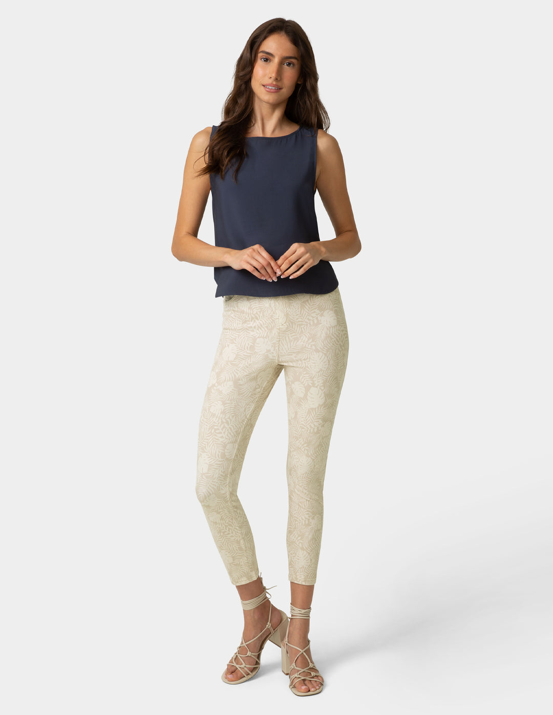Woman wearing a navy sleeveless top and beige patterned pants on a white background