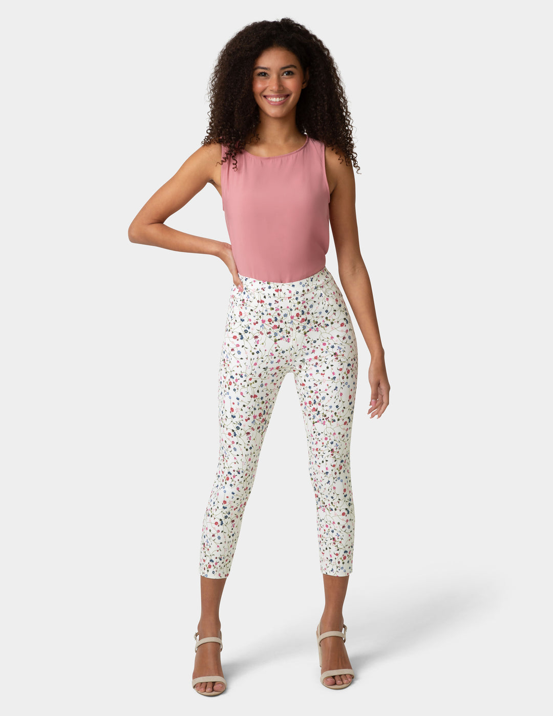 Woman wearing a pink sleeveless top and white floral pants on a white background