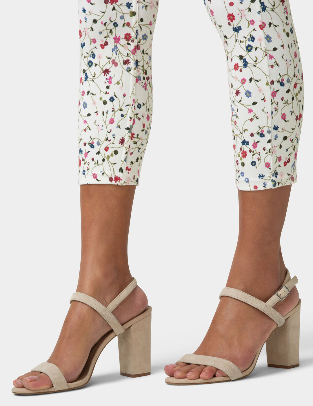 Beige high-heeled sandals worn with floral pants on a white background