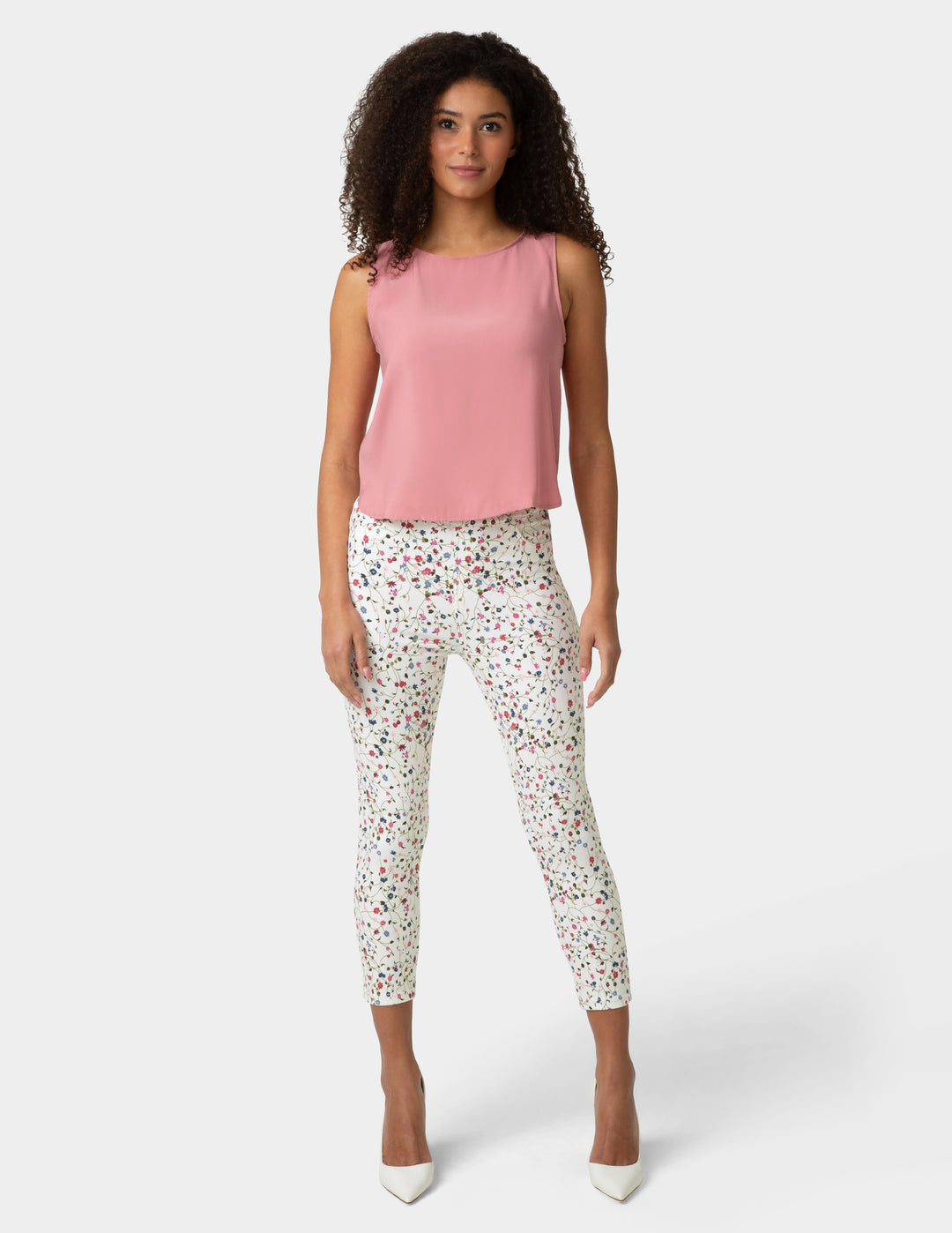 Woman wearing a pink sleeveless top and patterned pants on a white background