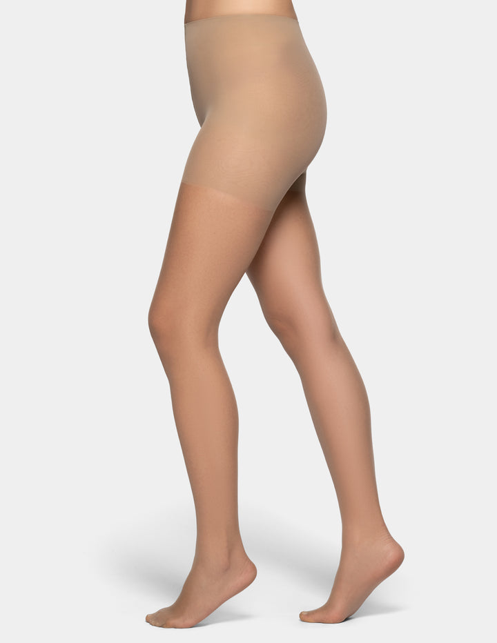 Side view of a model's legs wearing sheer beige hosiery/tights against a plain light gray background.
