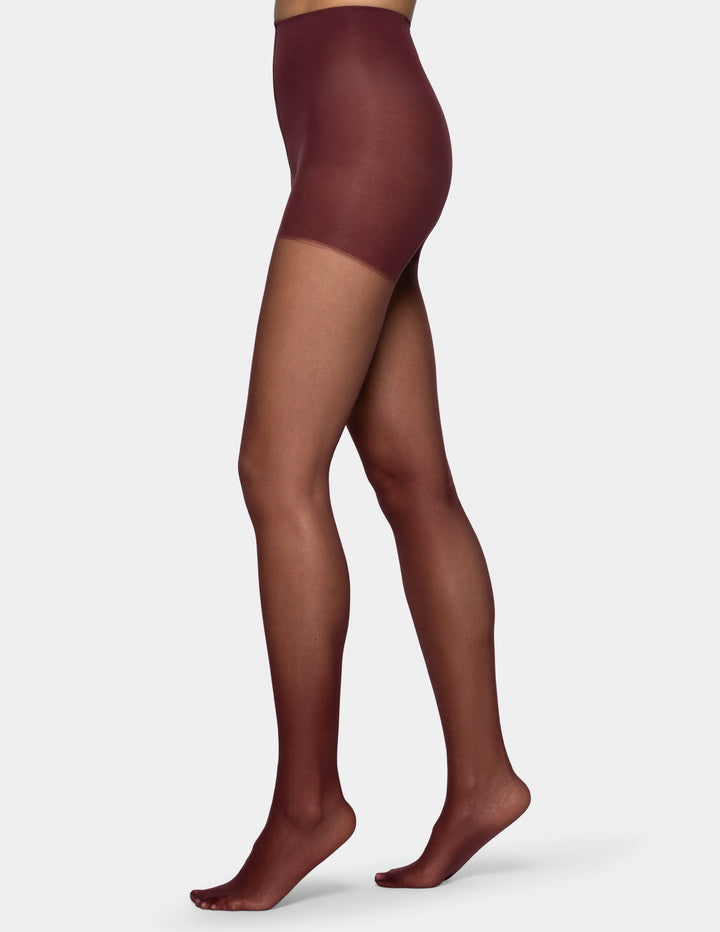 A side view of a model's legs wearing sheer burgundy tights set against a plain light gray background.