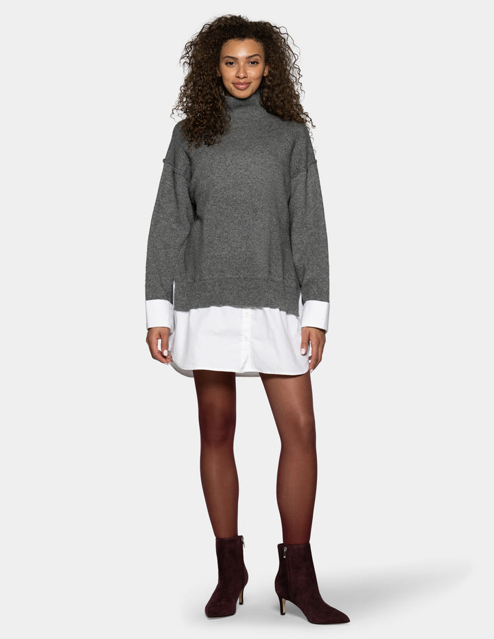 A model wearing a gray turtleneck sweater with white contrast cuffs, layered over a white shirt dress, paired with burgundy tights and dark brown heeled ankle boots, against a light gray background.