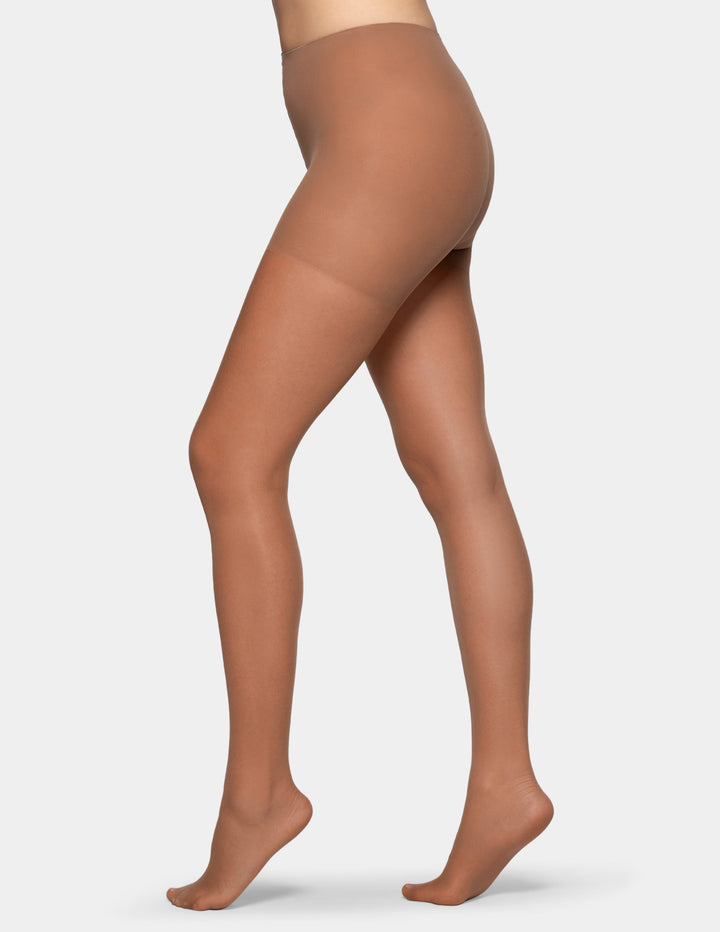 A model's legs wearing sheer, skin-toned hosiery tights, shown from the waist down against a light gray background.
