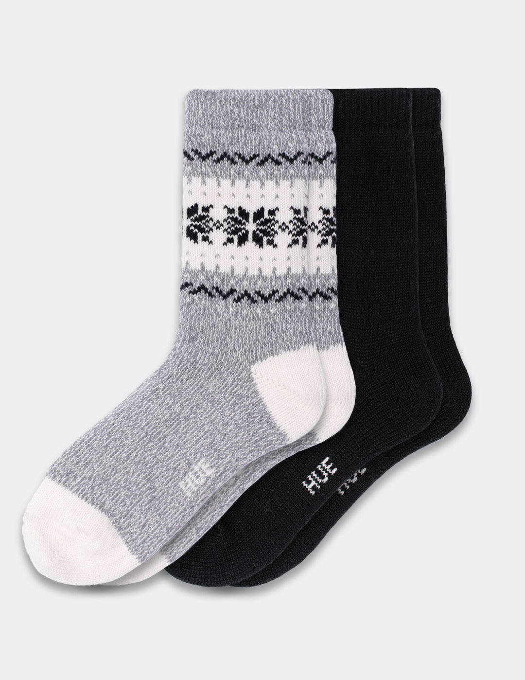 A 2-pack of crew socks by HUE, featuring one gray sock with a white and black Nordic snowflake pattern and one solid black sock, displayed on a light gray background.
