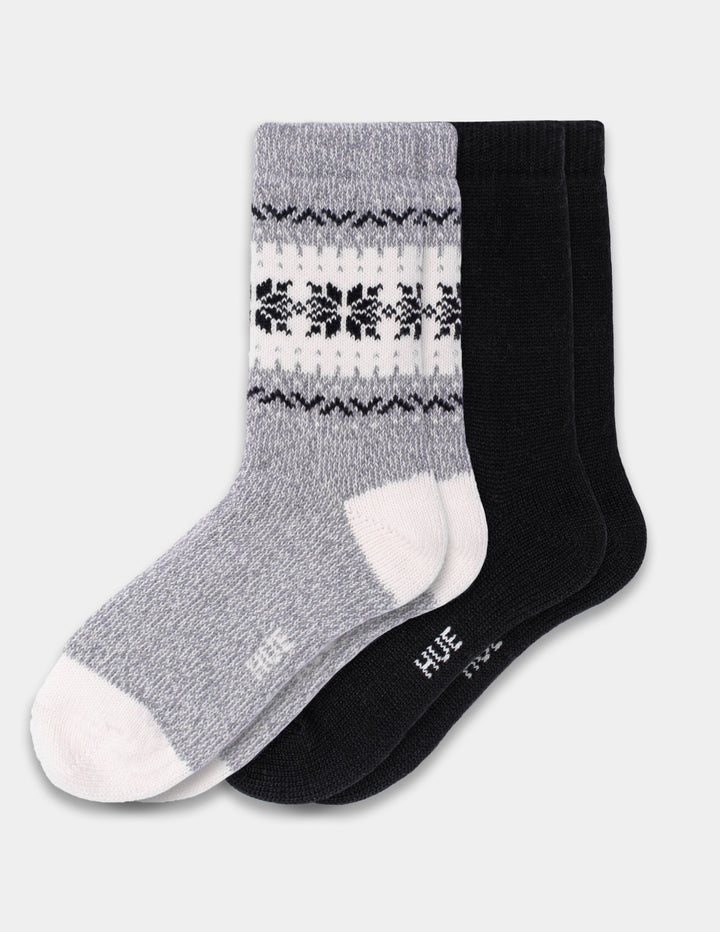 A 2-pack of crew socks by HUE, featuring one gray sock with a white and black Nordic snowflake pattern and one solid black sock, displayed on a light gray background.