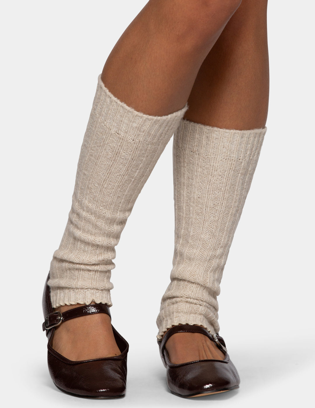 A model wearing light beige leg warmers and dark brown Mary Jane flats against a light gray background.
