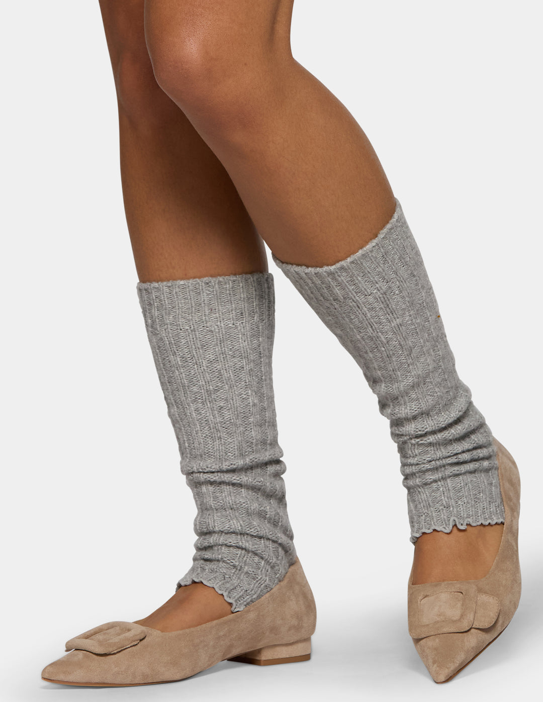 A model wearing light grey leg warmers and tan flats against a light gray background.