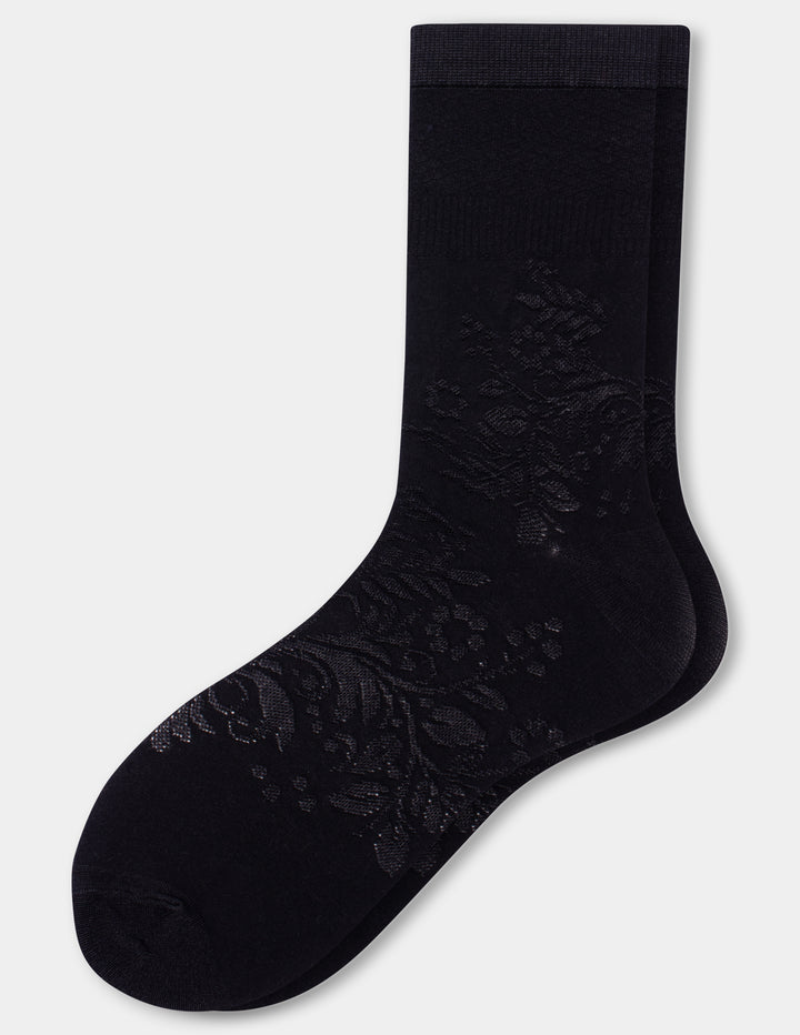 A pair of black crew socks with an intricate floral lace pattern on the foot, displayed against a light gray background.