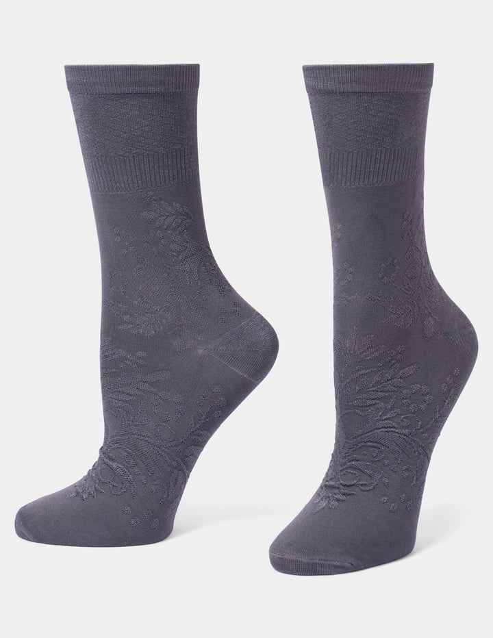 A pair of dark gray crew socks with a subtle tonal floral jacquard pattern, displayed on foot forms against a light gray background.