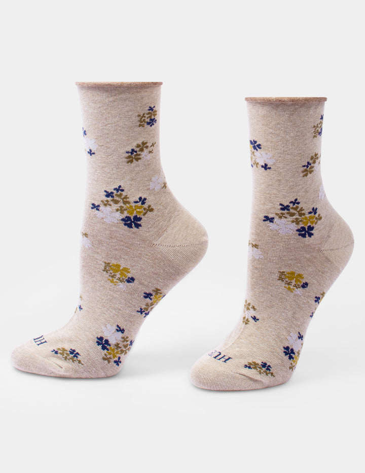 A pair of crew socks in a heathered beige color, featuring a scattered floral pattern with blue, yellow, and white blossoms, displayed on foot forms against a light gray background.