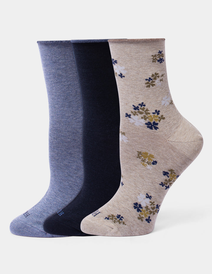 Three pairs of crew socks against a light gray background. The left pair is heathered medium blue, the middle pair is solid navy, and the right pair is heathered beige with a small blue and mustard yellow floral pattern.