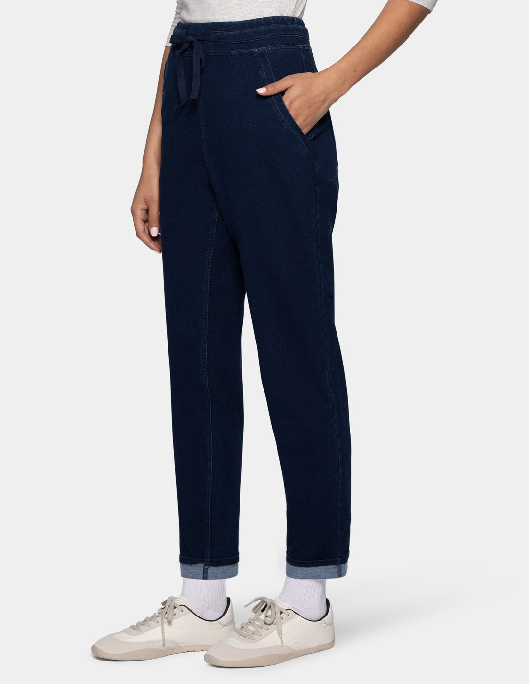 A person wearing dark blue drawstring joggers with side pockets, paired with white socks and off-white sneakers, shown from the waist down against a light gray background.