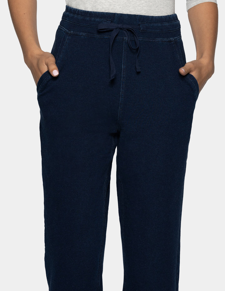 A close-up of a person wearing dark blue joggers with a drawstring waistband and side pockets, paired with a light gray top, against a plain light gray background.