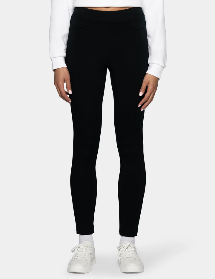 A model wearing black full-length leggings, styled with a white long-sleeve crop top and white sneakers, shown from the waist down against a light gray background.
